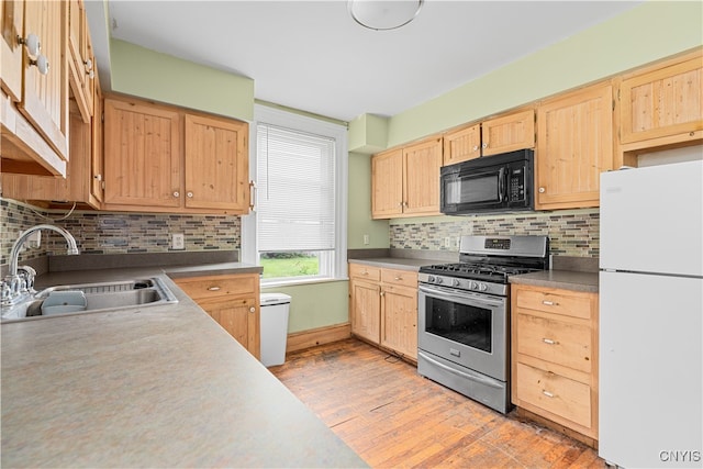 kitchen featuring white refrigerator, sink, stainless steel gas stove, light wood-type flooring, and tasteful backsplash