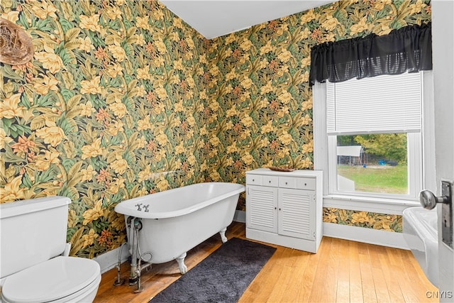 bathroom with a washtub, hardwood / wood-style flooring, and toilet