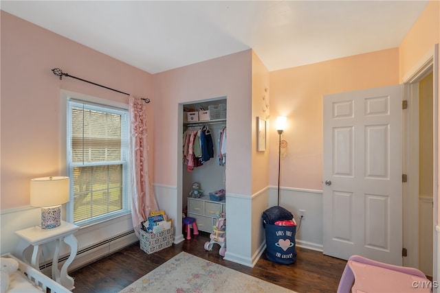 bedroom with dark hardwood / wood-style flooring, baseboard heating, and a closet