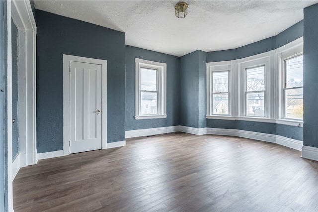 unfurnished room with a textured ceiling, plenty of natural light, and dark wood-type flooring