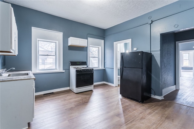 kitchen with white gas stove, black fridge, sink, and a wealth of natural light