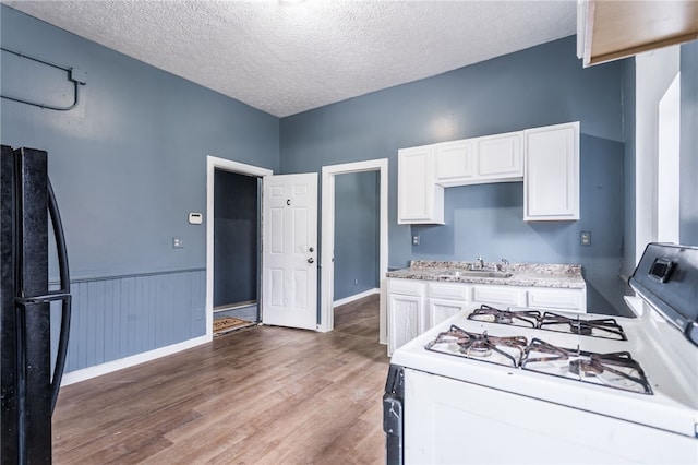 kitchen featuring white gas range, white cabinetry, a textured ceiling, black refrigerator, and hardwood / wood-style flooring