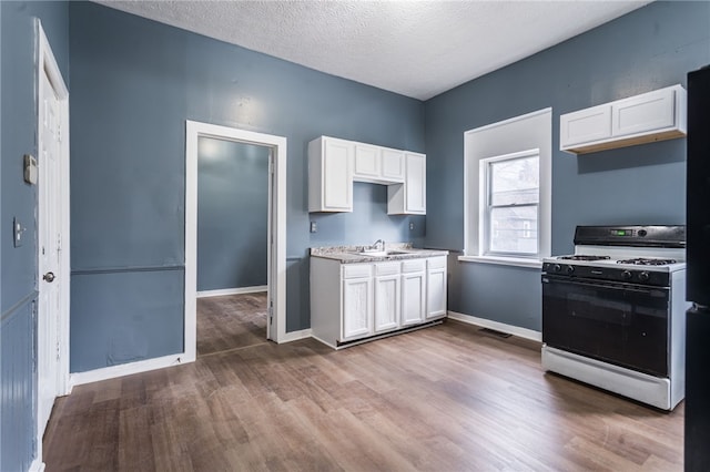 kitchen with a textured ceiling, sink, hardwood / wood-style flooring, white range with gas stovetop, and white cabinetry