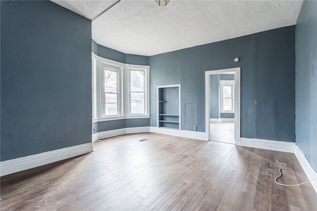 unfurnished room with built in shelves, wood-type flooring, and a textured ceiling