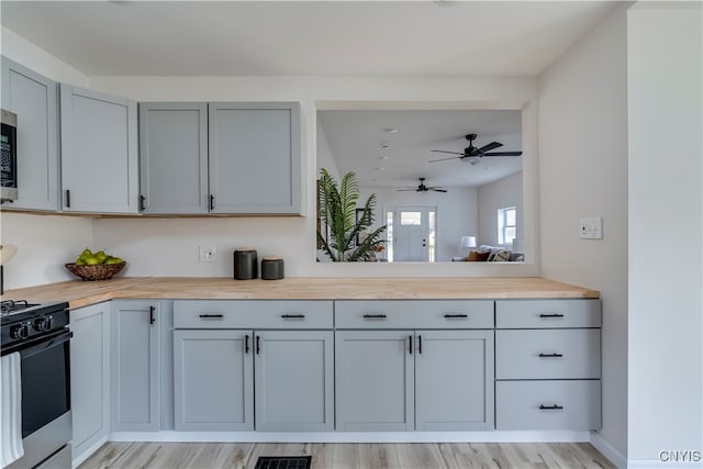 kitchen featuring wooden counters, light wood-type flooring, gray cabinetry, range with gas cooktop, and ceiling fan