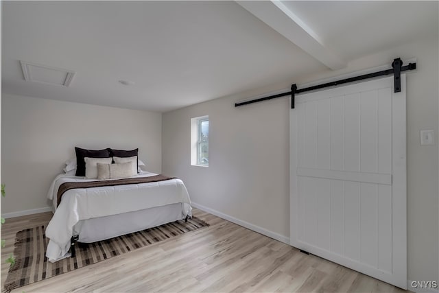 bedroom with beam ceiling, a barn door, and light hardwood / wood-style floors