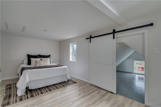 bedroom featuring light wood-type flooring, lofted ceiling with beams, and a barn door