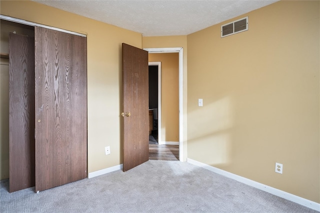 unfurnished bedroom featuring light carpet, a textured ceiling, and a closet