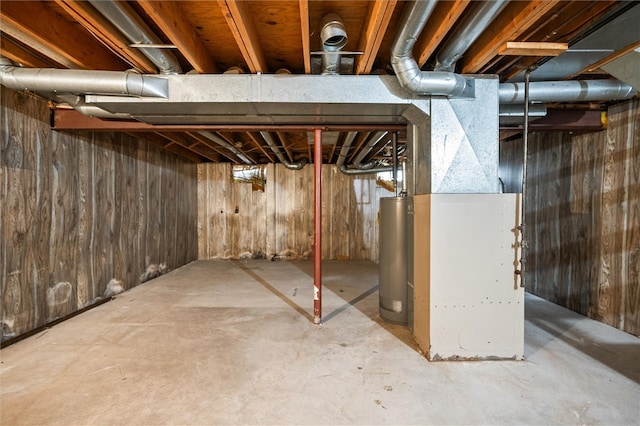 basement featuring water heater and wood walls