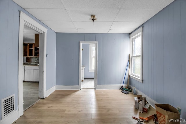 unfurnished room with wood walls, a drop ceiling, and light hardwood / wood-style floors