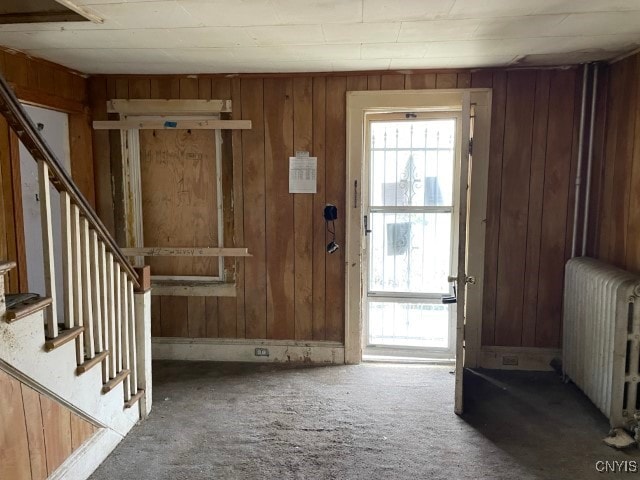 carpeted entryway featuring radiator heating unit and wooden walls