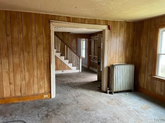 spare room featuring carpet flooring, radiator heating unit, and wood walls