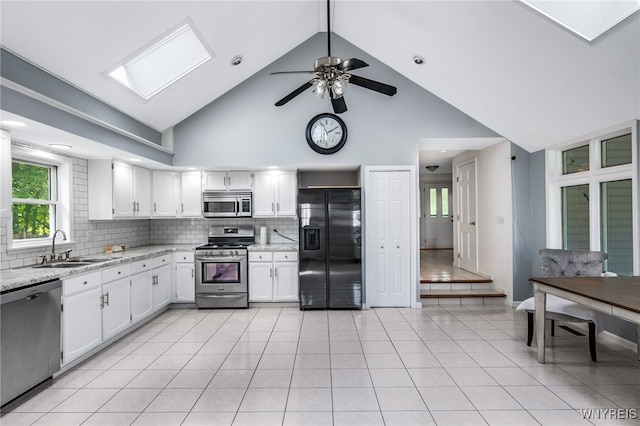 kitchen with appliances with stainless steel finishes, high vaulted ceiling, white cabinetry, and sink