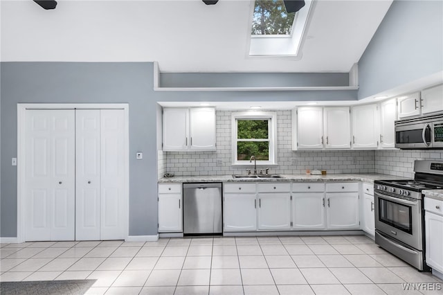 kitchen featuring sink, stainless steel appliances, light tile patterned floors, high vaulted ceiling, and white cabinets