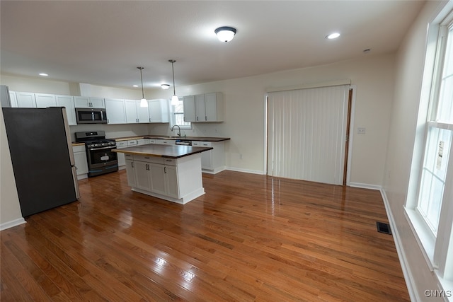 kitchen with pendant lighting, a center island, white cabinets, appliances with stainless steel finishes, and dark hardwood / wood-style flooring