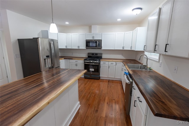 kitchen with wooden counters, appliances with stainless steel finishes, light hardwood / wood-style flooring, white cabinets, and hanging light fixtures