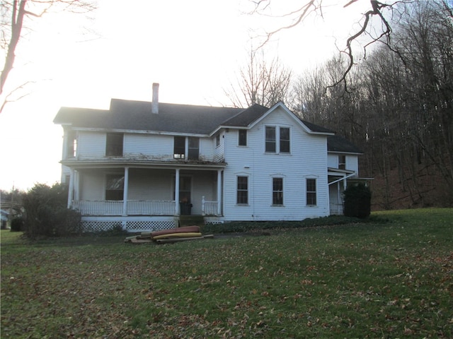 rear view of property featuring covered porch and a yard