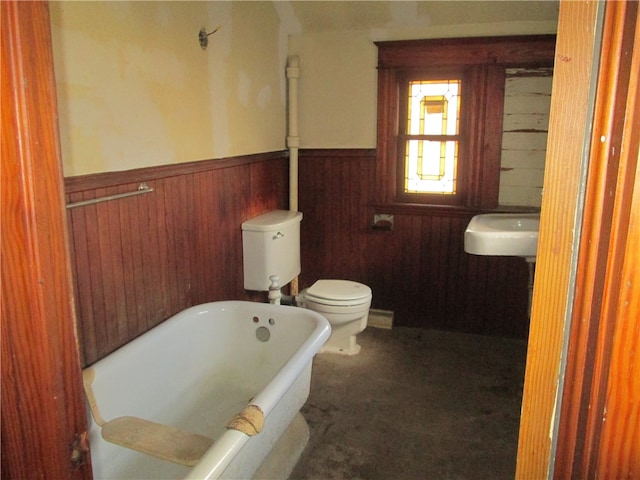 bathroom with a tub to relax in, toilet, wooden walls, and sink