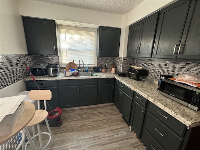 kitchen with light stone countertops, light wood-type flooring, tasteful backsplash, a textured ceiling, and sink