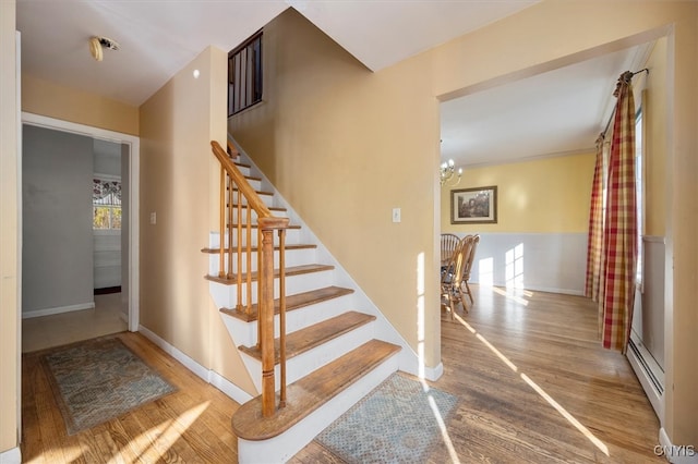 stairs featuring hardwood / wood-style flooring, baseboard heating, and an inviting chandelier