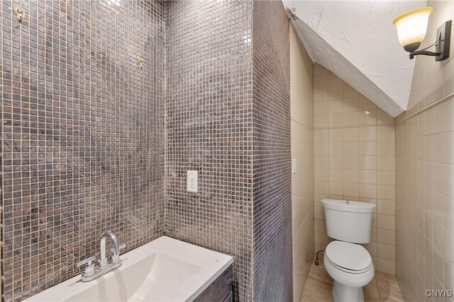 bathroom with tile patterned flooring, toilet, sink, and tile walls