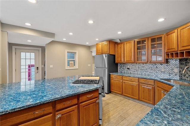 kitchen with appliances with stainless steel finishes, light wood-type flooring, backsplash, dark stone counters, and sink