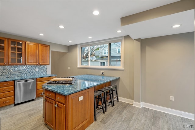 kitchen featuring dishwasher, light wood-type flooring, a breakfast bar, and dark stone counters