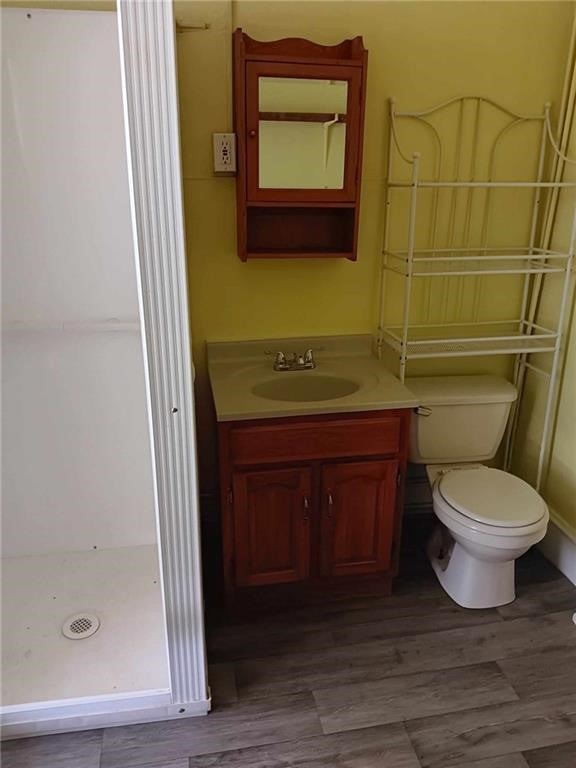 bathroom with a shower, hardwood / wood-style floors, vanity, and toilet