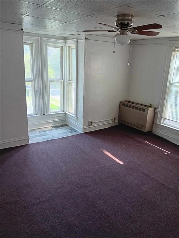 carpeted empty room featuring a drop ceiling, an AC wall unit, and ceiling fan