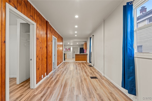 hall featuring wooden walls, light hardwood / wood-style flooring, and ornamental molding