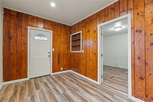 foyer with wood walls, ornamental molding, and light wood-type flooring