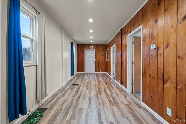 hallway featuring wooden walls, crown molding, and light wood-type flooring