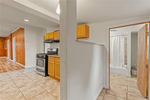 kitchen featuring light tile patterned flooring, crown molding, wood walls, and stainless steel gas range