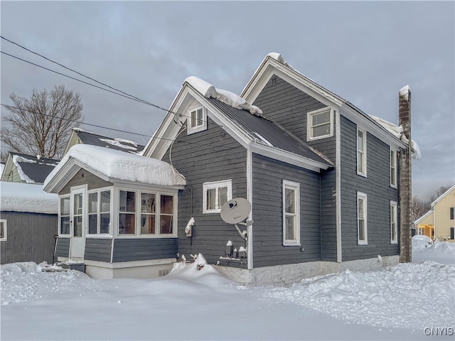 snow covered rear of property featuring a sunroom