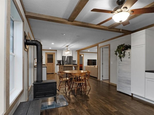 dining space featuring ceiling fan, a wood stove, dark hardwood / wood-style floors, a textured ceiling, and beamed ceiling