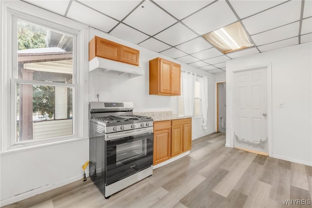 kitchen with light stone countertops, stainless steel gas stove, light hardwood / wood-style floors, and a paneled ceiling