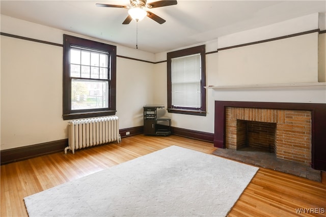 unfurnished living room with ceiling fan, wood-type flooring, a fireplace, and radiator