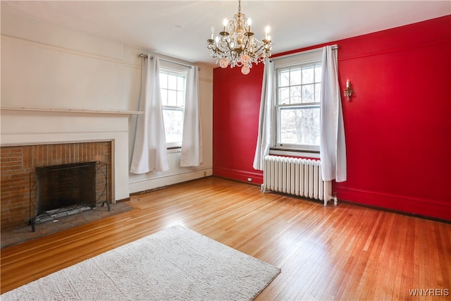 unfurnished living room with radiator, a baseboard radiator, a brick fireplace, an inviting chandelier, and hardwood / wood-style flooring