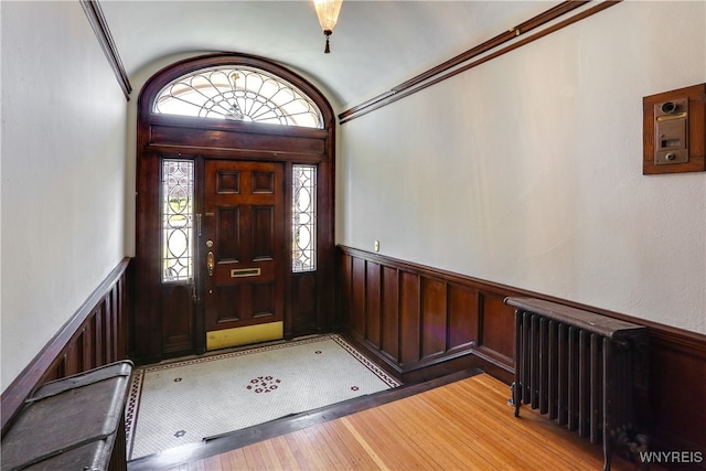 foyer entrance featuring light hardwood / wood-style floors, radiator, and wood walls