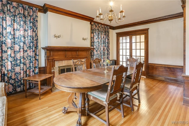 dining space with crown molding, light hardwood / wood-style flooring, a chandelier, and a brick fireplace