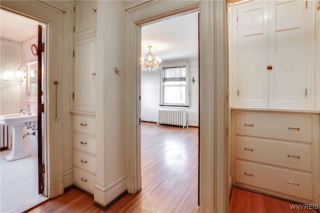 corridor with sink, radiator heating unit, a notable chandelier, and light wood-type flooring