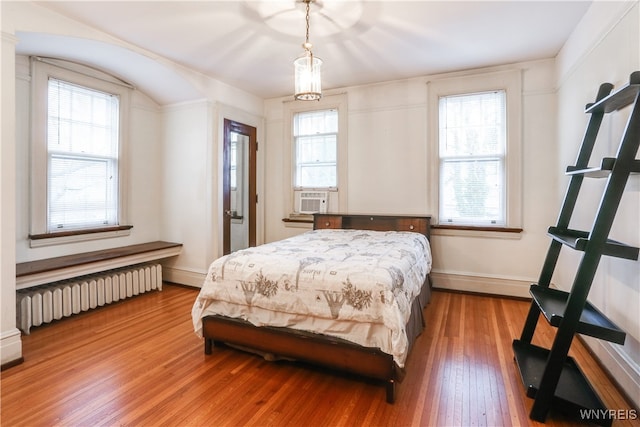 bedroom featuring radiator heating unit, multiple windows, cooling unit, and hardwood / wood-style floors