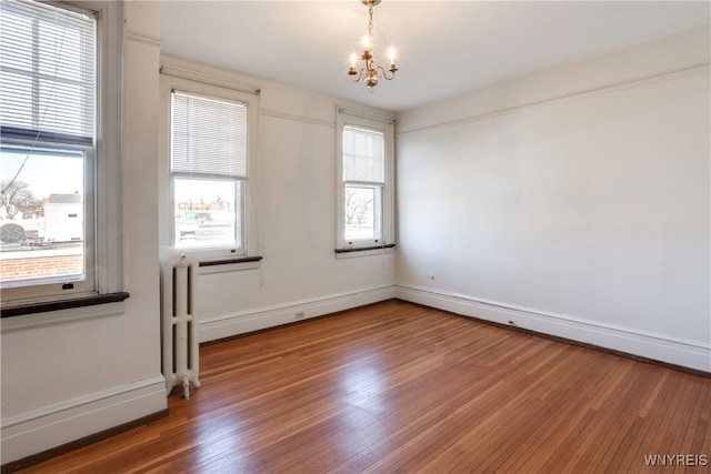 unfurnished room featuring wood-type flooring, an inviting chandelier, and radiator