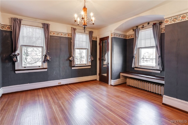 empty room featuring hardwood / wood-style floors, a healthy amount of sunlight, radiator, and an inviting chandelier