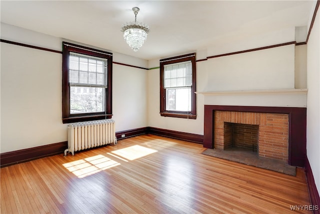 unfurnished living room featuring a chandelier, light hardwood / wood-style flooring, radiator, and a fireplace