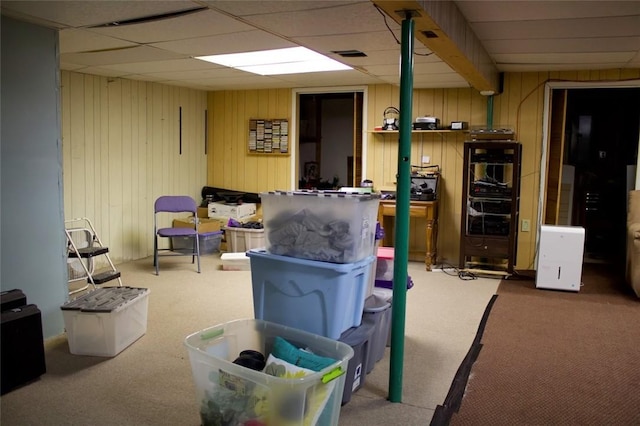 basement featuring carpet, a drop ceiling, and wood walls