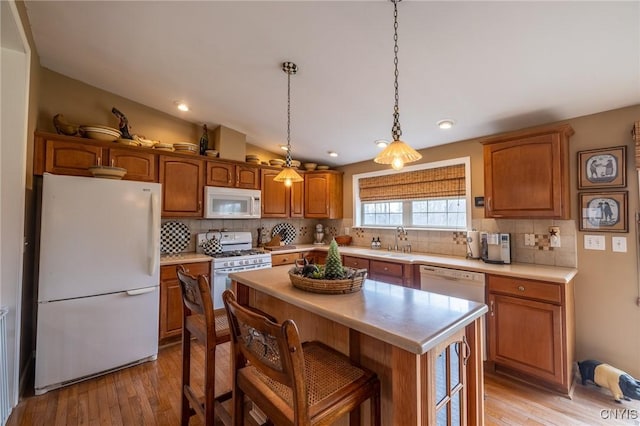 kitchen with tasteful backsplash, white appliances, sink, a center island, and light hardwood / wood-style floors