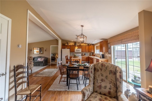 dining area with a chandelier, lofted ceiling with beams, and light hardwood / wood-style flooring