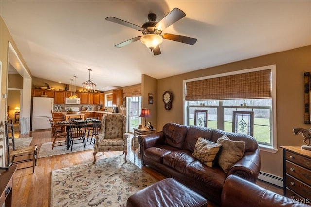 living room featuring ceiling fan with notable chandelier, a baseboard heating unit, lofted ceiling, and light hardwood / wood-style flooring