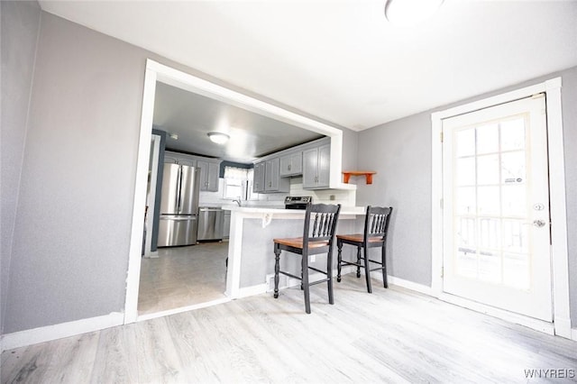 kitchen featuring gray cabinetry, stainless steel appliances, light hardwood / wood-style flooring, kitchen peninsula, and a kitchen bar